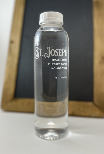 Bottle of St. Joseph Water standing on a wooden crate against a dark wall
